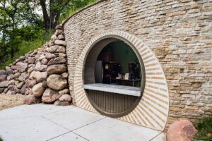 Circular service window set into a stone wall, with a counter and beverage machines inside.