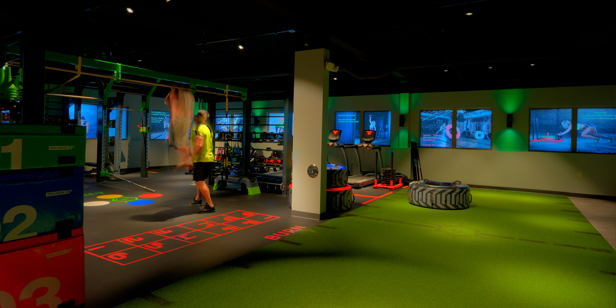 Training studio at Carbon World Health with turf floor, tire flip stations, numbered training zones, and video wall display