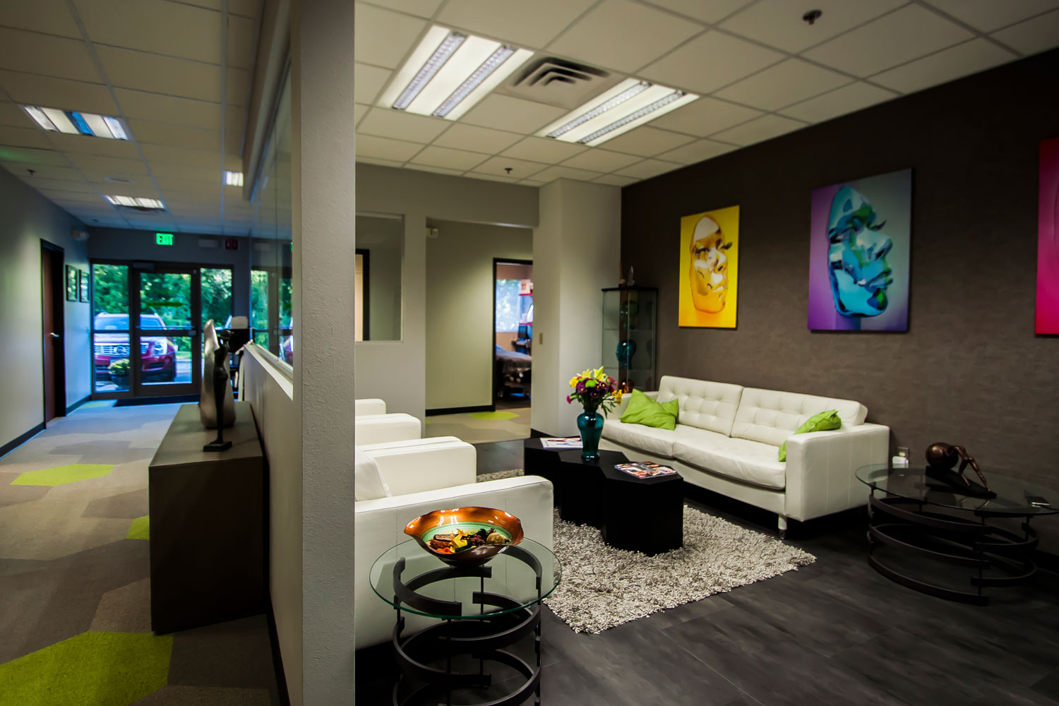 Reception lounge at Carbon World Health with white sofas, colorful artwork, dark accent wall, and view to entry corridor