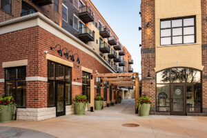 Corner view of Middleton Center brick building with pergola entry, upper-floor balconies, and retail storefronts at street level