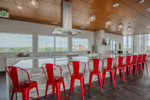 Community lounge at Peloton Residences with red bar stools, stone accent wall, wood ceiling, and views to the kitchen area