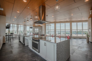 Community kitchen at Peloton Residences with large island, wood ceiling, globe pendant lighting, and floor-to-ceiling windows overlooking the lake