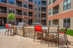Outdoor amenity courtyard at Peloton Residences with built-in grills, stone bar surround, and red patio chairs