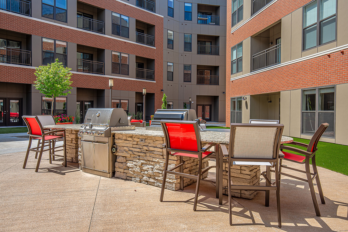 Outdoor amenity courtyard at Peloton Residences with built-in grills, stone bar surround, and red patio chairs