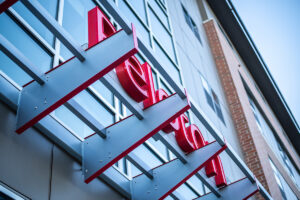 Close-up of red Peloton Residences building signage mounted on glass curtain wall facade
