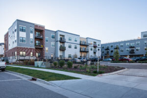 Side exterior view of Lamphouse with gray and brick facade, upper-floor balconies, and surface parking lot
