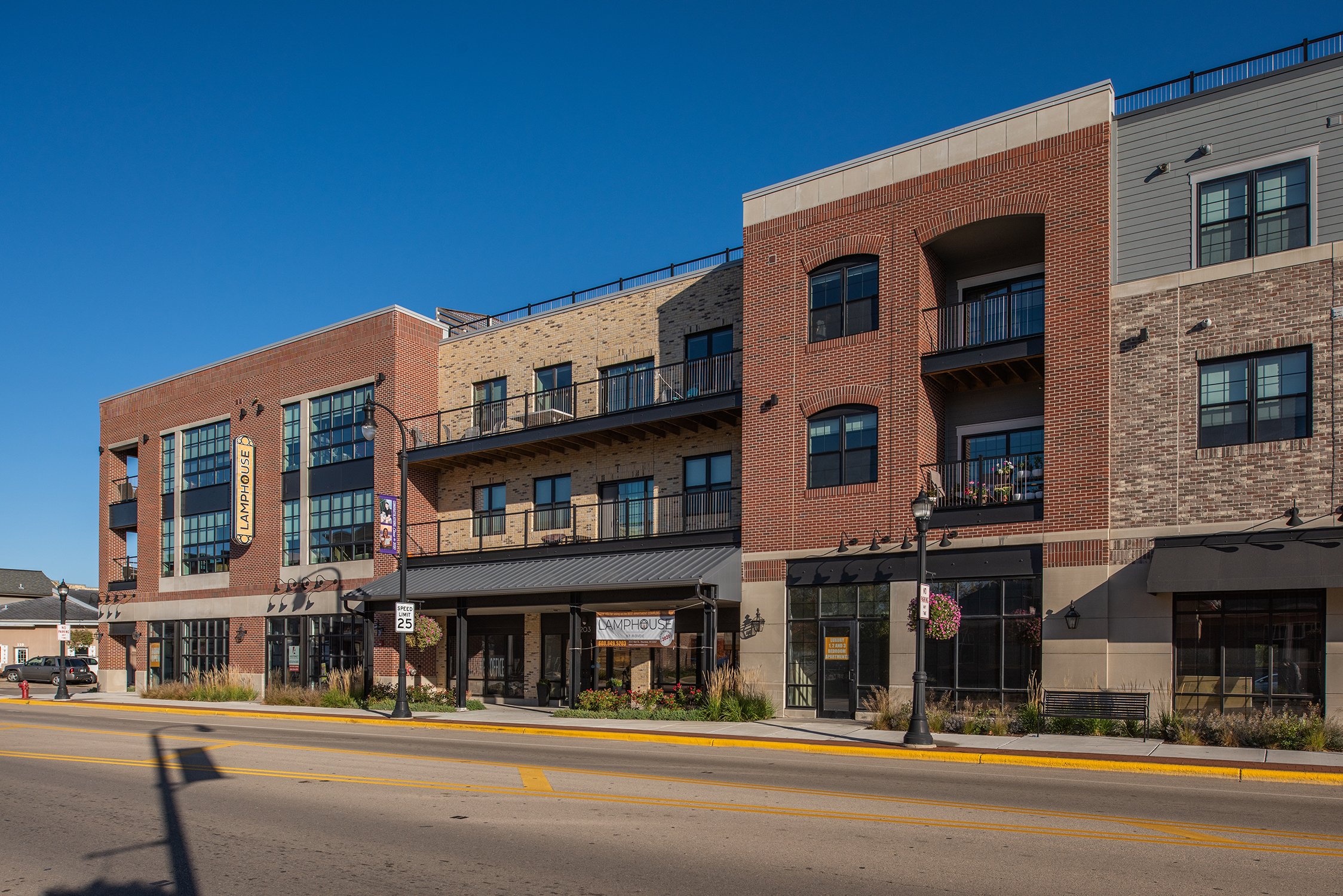 Street-level exterior of Lamphouse with brick and tan facade, retail storefronts, Lamphouse signage, and upper-floor balconies