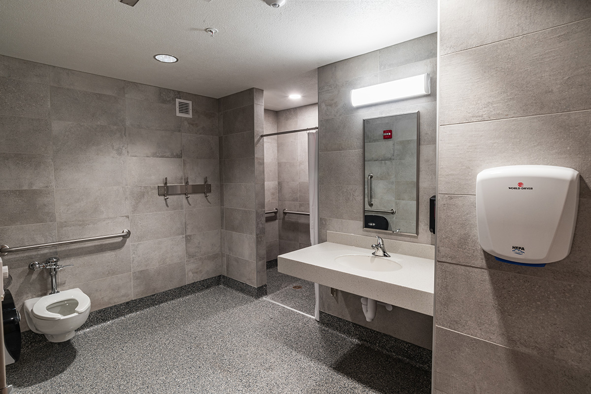 Accessible bathroom at Beloit College Whitney Hall with tile walls, grab bars, wall-mounted sink, and hand dryer