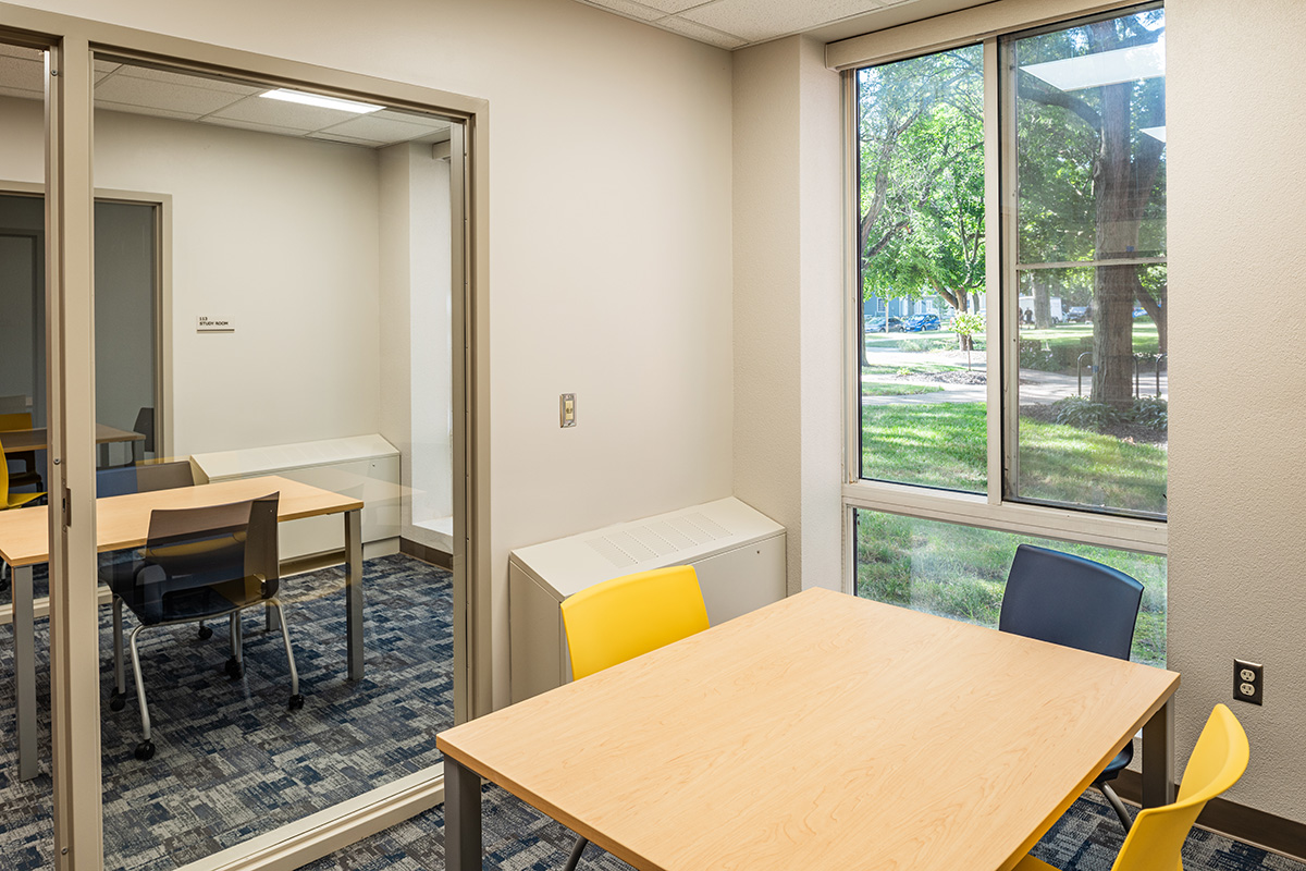 Study room at Beloit College Whitney Hall with table, yellow chairs, glass partition wall, and windows overlooking campus
