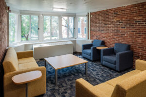 Student lounge at Beloit College Whitney Hall with sofas, armchairs, exposed brick wall, and large windows