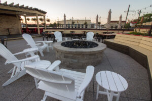 Rooftop patio fire pit at Village Crossing surrounded by white Adirondack chairs and dining tables at dusk