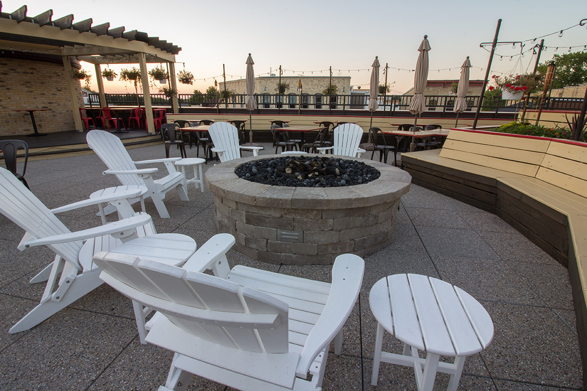 Rooftop patio fire pit at Village Crossing surrounded by white Adirondack chairs and dining tables at dusk