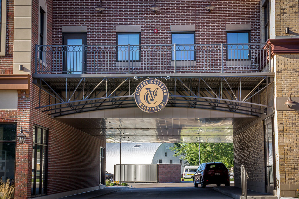 Village Crossing Gateway Arch and Signage Village Crossing gateway arch with round medallion signage over a drive-through passage between brick buildings in Waunakee Wisconsin