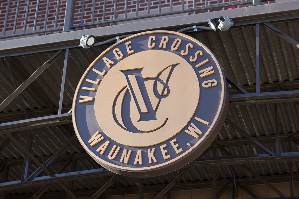 Close-up of Village Crossing Waunakee Wisconsin medallion signage mounted on steel truss structure